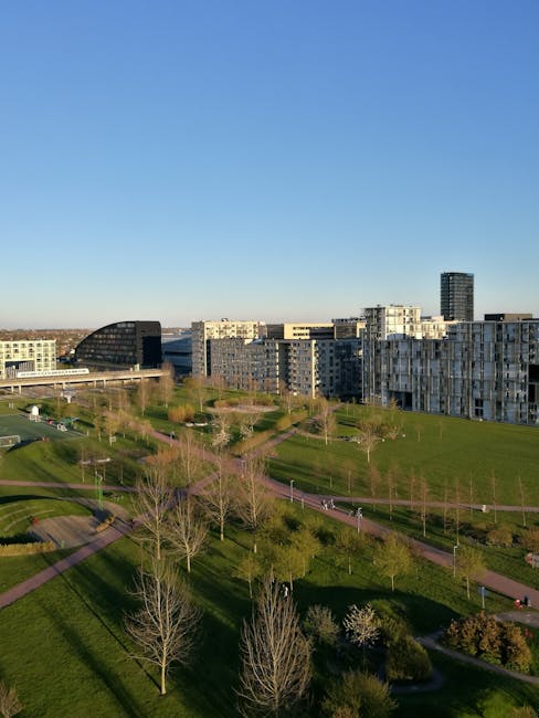 A busy urban street scene in Brent Cross featuring a corner building with a classic architectural design, including white decorative trim and large windows on the upper floors, and a pub named 'The World's End' situated on the ground floor. The street is active with pedestrians walking on the sidewalks, some crossing the road at a pedestrian crossing with a green signal, and vehicles including cars and a bus moving along the road. In the foreground, there are several wooden crates placed on the paved pavement, which appears to be part of a home relocation or moving process. The scene is captured during daytime with partly cloudy skies, and street furniture such as lampposts and traffic lights are visible, along with some overhead tram or trolleybus wires. The image is relevant to house removals and furniture transport, illustrating the logistical environment surrounding property moves, as seen through the exterior of a typical NW4 West London street, supported by [COMPANY_NAME] in providing professional removal services.